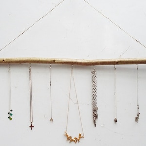 May include: A wooden branch with six necklaces hanging from it. The necklaces are made of silver, gold, and a mix of green and blue stones.