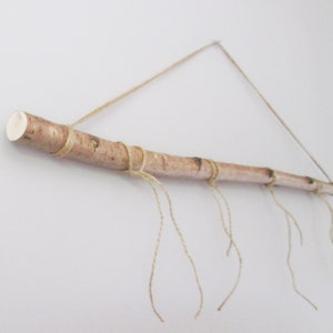 May include: A natural wood branch with twine wrapped around it, hanging from the ceiling. The twine is tied in knots and hangs down from the branch, creating a rustic and decorative look.