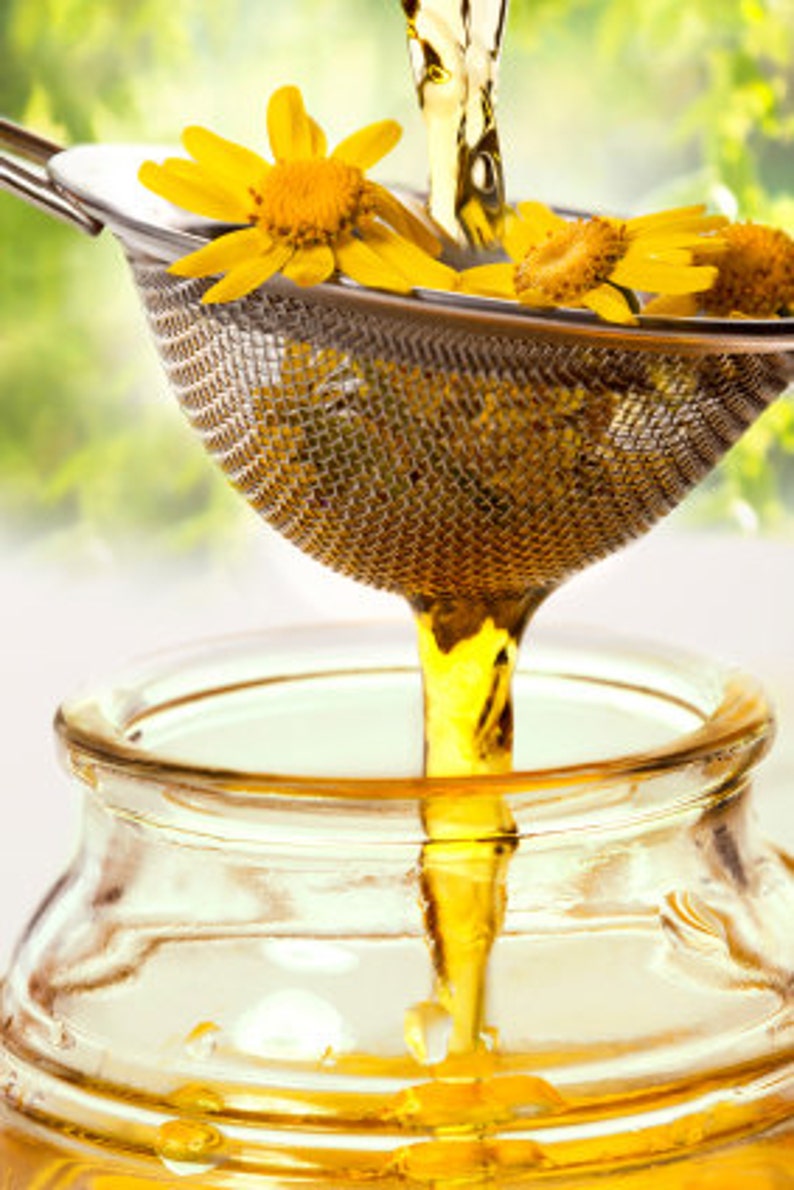 May include: A clear glass jar filled with golden liquid.  A strainer with yellow flowers is pouring the liquid into the jar.