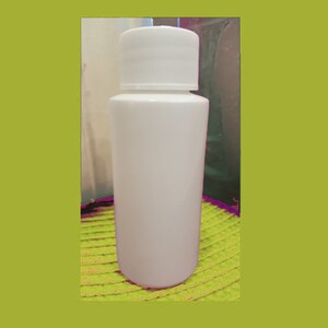 May include: White plastic bottle with a white screw-on lid. The bottle is sitting on a green and yellow surface.
