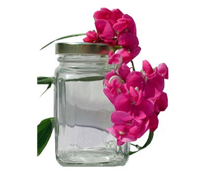 Puede incluir: Un tarro de vidrio transparente con tapa dorada, lleno de un l&iacute;quido transparente. Un racimo de flores de guisante dulce rosas se apoya en el tarro.