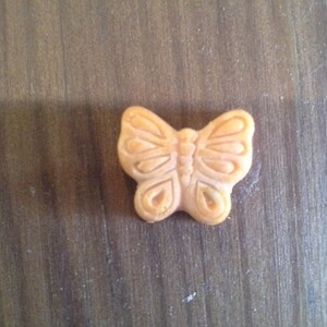 Puede incluir: Un peque&ntilde;o amuleto de mariposa de color naranja con detalles intrincados.