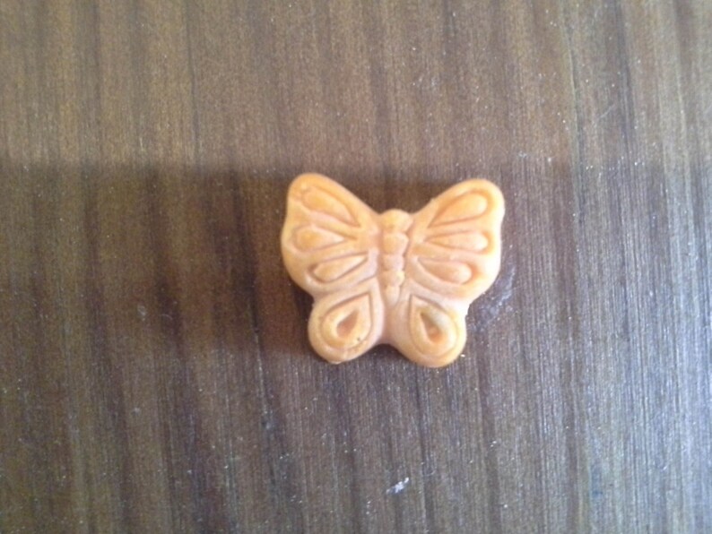 Puede incluir: Un peque&ntilde;o amuleto de mariposa de color naranja con detalles intrincados.