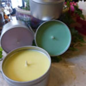 May include: Three candles in silver tins. The candles are yellow, green, and purple.