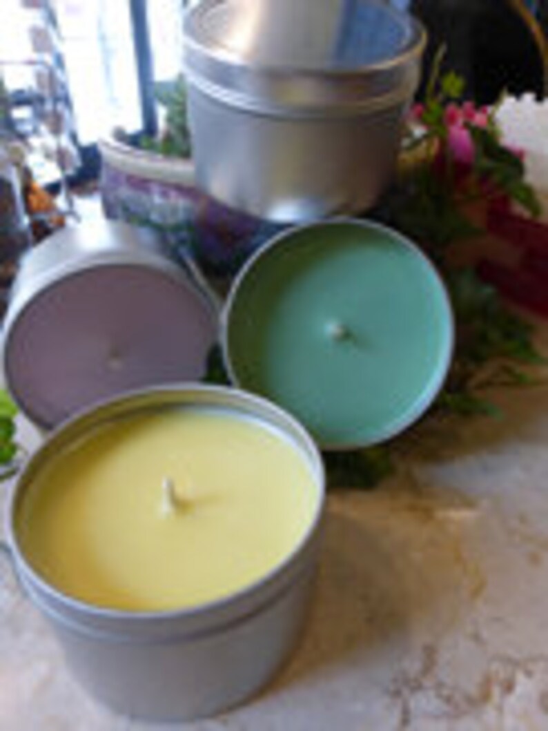May include: Three candles in silver tins. The candles are yellow, green, and purple.
