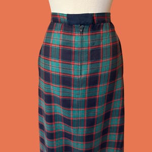May include: A plaid pencil skirt in a classic tartan pattern. The skirt features a navy blue, green, and red color scheme. It has a zipper closure at the back and a navy blue waistband. The skirt is displayed on a mannequin.