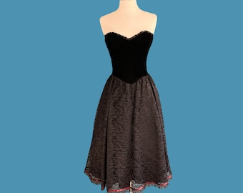 May include: A black strapless dress with a velvet bodice and a lace skirt. The skirt has a scalloped hemline and a red ribbon trim.