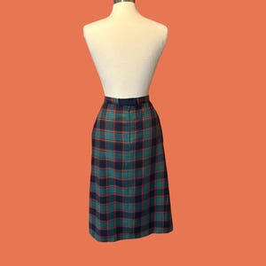 May include: A vintage plaid skirt in shades of green, navy, and red, displayed on a mannequin. The skirt features a classic plaid pattern and a tailored fit, perfect for a retro or preppy style.