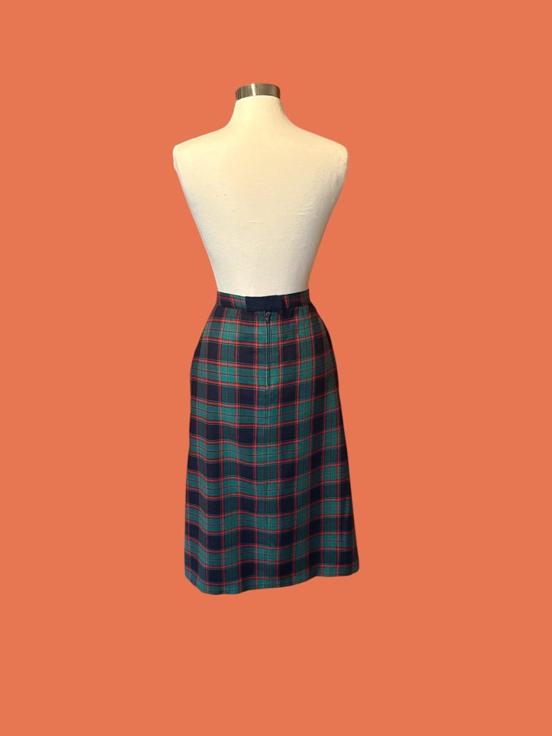 May include: A vintage plaid skirt in shades of green, navy, and red, displayed on a mannequin. The skirt features a classic plaid pattern and a tailored fit, perfect for a retro or preppy style.