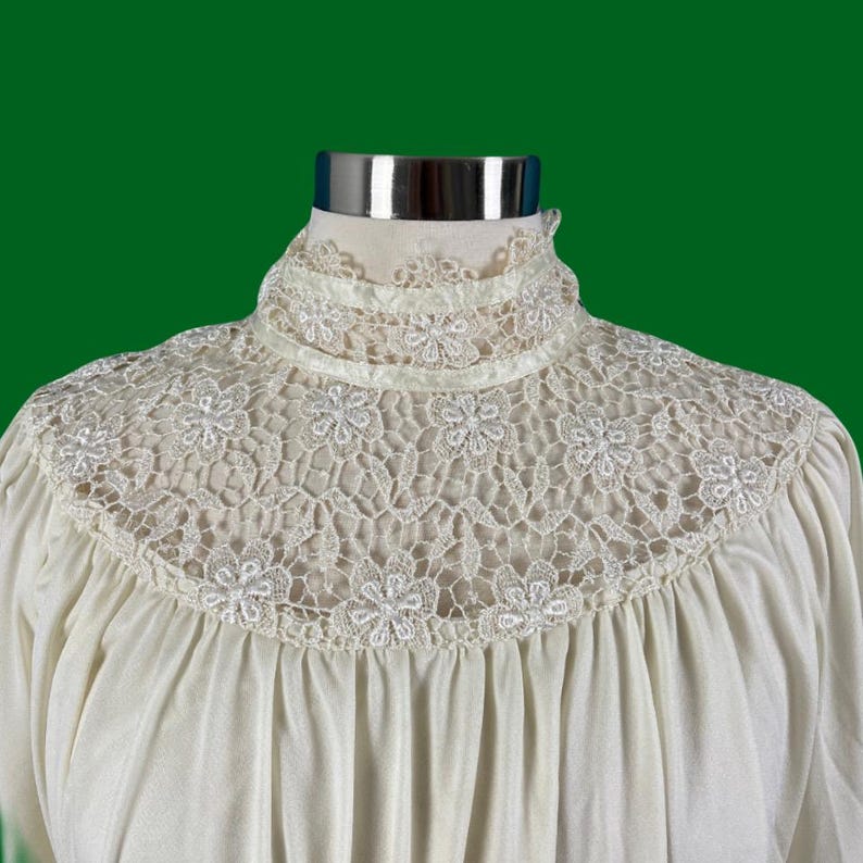 Pode incluir: Uma blusa branca com gola alta e uma delicada renda. A renda &eacute; um padr&atilde;o floral e &eacute; muito detalhada.