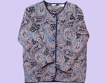Könnte beinhalten: Marineblaue Strickjacke mit Paisley-Muster in Blau- und Mauve-Tönen. Das langärmlige Oberteil hat eine dunkelmarinefarbene Paspelierung und einen V-Ausschnitt. Das Kleidungsstück ist aus einem weichen, möglicherweise gewebten Stoff.