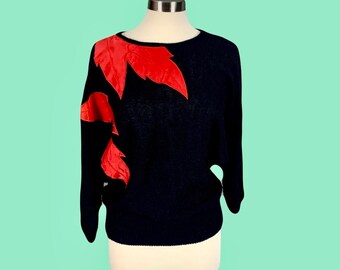 May include: A black sweater with red leather leaf appliques. The sweater has a round neckline and long sleeves.