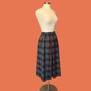 May include: A vintage plaid skirt in green, navy, and red, displayed on a mannequin. The skirt has a pleated design and falls to a mid-calf length. The fabric features a classic tartan pattern, showcasing a timeless style.
