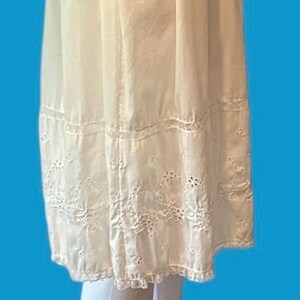May include: Cream-colored, vintage-style skirt with intricate eyelet embroidery along the hemline. The skirt features a tiered design with delicate stitching and a scalloped edge, suggesting a romantic, feminine aesthetic.