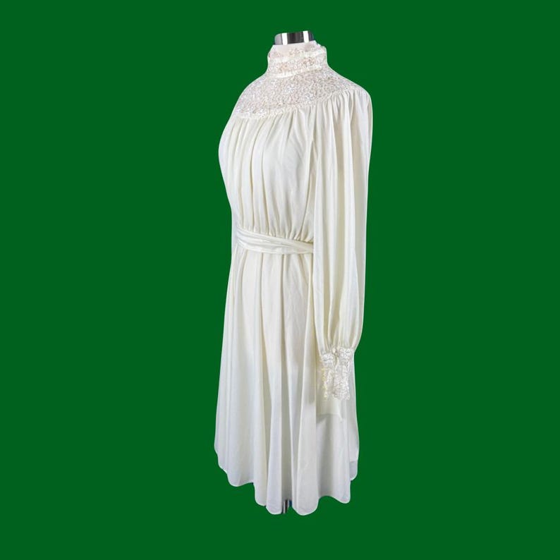 Pode incluir: Um vestido branco de manga comprida com gola alta e acabamento em renda. O vestido tem um corpete justo e uma saia fluida.