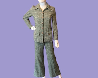 May include: A vintage green tweed suit, comprising a collared jacket with four pockets and matching flared trousers. The jacket features button closures. The suit is displayed on a mannequin against a purple backdrop.
