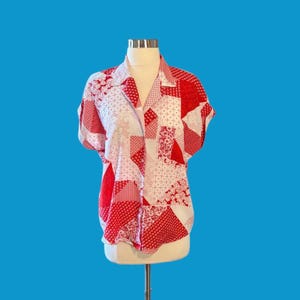May include: A short-sleeved, collared shirt with a patchwork design in red and white. The shirt features various patterns, including polka dots, floral prints, and geometric shapes. The shirt is displayed on a mannequin against a blue background.