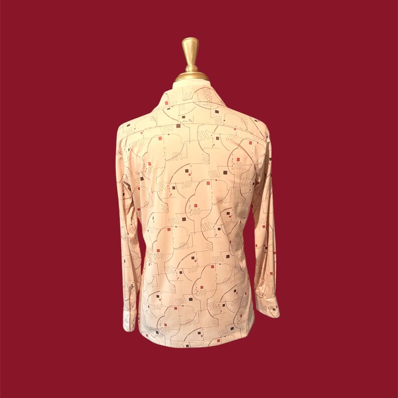 May include: A long-sleeved button-down shirt with a cream-colored background and a repeating pattern of abstract shapes in black, red, and brown. The shirt is displayed on a mannequin against a deep red backdrop.