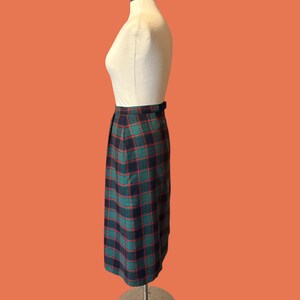 May include: A vintage plaid skirt in shades of navy, green, and red, displayed on a mannequin. The skirt features a classic plaid pattern and a tailored silhouette. The skirt is knee-length and has a belt detail at the waist.