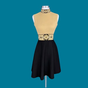 May include: A sleeveless dress with a black skirt and a beige top. The top has a gold and black patterned band around the waist.