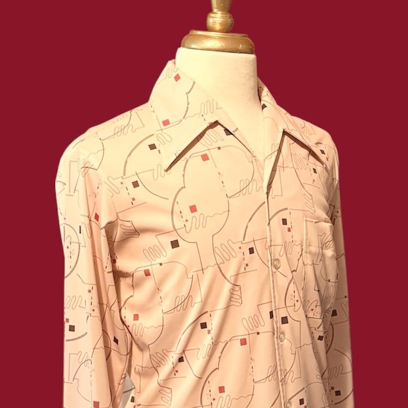 May include: A cream-colored button-down shirt with a geometric pattern of brown lines and red and brown squares. The shirt has a classic collar and a single chest pocket. The shirt is displayed on a mannequin.