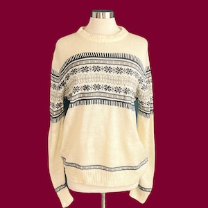 May include: A cream-coloured sweater with a black and grey snowflake pattern. The sweater has long sleeves and a crew neck.
