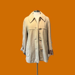 Peut inclure: Une veste en laine beige avec un col, quatre boutons et une doublure à carreaux sur les poignets.