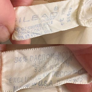 May include: Close-up of two cream-colored fabric tags. The top tag has the word "LEAD" printed in blue, along with other text and numbers. The bottom tag has text that includes "34% DACRON-POLY" and "MADE IN U.S.A." in blue.