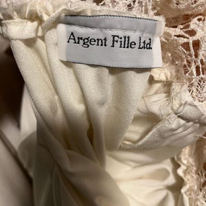 Pode incluir: Um top branco de renda com uma etiqueta branca que diz "Argent Fille Ltd."