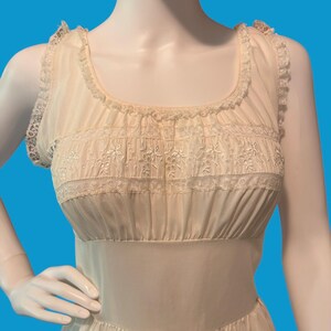 May include: Cream-colored vintage nightgown with delicate lace trim and floral embroidery. The sleeveless gown features a scoop neckline and a fitted bodice with horizontal gathering. The fabric appears lightweight and semi-sheer, with a subtle sheen.