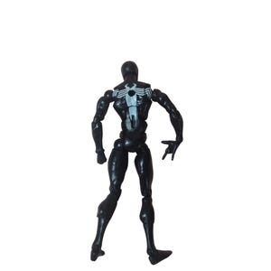 Peut inclure: Figurine d'action noire d'un super-h&eacute;ros, vue de dos. La figurine porte un embl&egrave;me d'araign&eacute;e blanc sur le dos et est pos&eacute;e avec une main ouverte. La figurine est articul&eacute;e au niveau des articulations.
