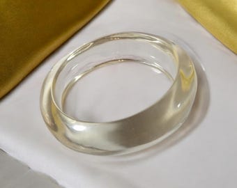 May include: A clear plastic bangle bracelet. The bracelet is thick and has a smooth, glossy finish.