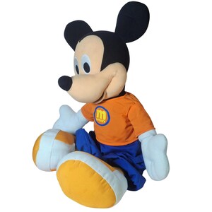 Pu&ograve; includere: Un peluche di Topolino con orecchie nere, naso nero e viso beige. Mickey indossa una maglietta arancione con un logo a cerchio blu e la scritta "Mickey". Indossa anche pantaloni blu e scarpe gialle e bianche.