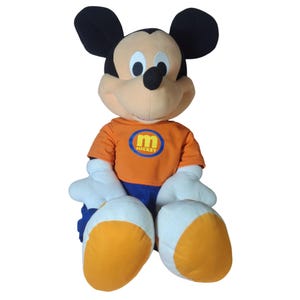 Pu&ograve; includere: Una grande bambola di peluche di Topolino. Mickey indossa una maglietta arancione con un logo "Mickey" blu e giallo, pantaloncini blu e guanti e scarpe bianche. La bambola ha orecchie nere e una faccia color camoscio.