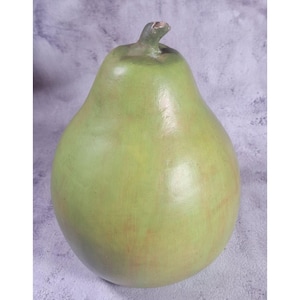 Puede incluir: Un objeto decorativo grande, hecho a mano, con forma de pera. La pera está pintada en tonos verdes con sutiles acentos marrón rojizo, y tiene un pequeño tallo texturizado. El diseño general es suave y redondeado, sugiriendo una forma natural y orgánica.