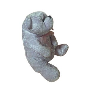 May include: A plush gray teddy bear with a pink bow tie. The bear is sitting with its legs crossed and its head tilted to the side.