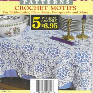 May include: A book cover with a white crocheted tablecloth on a blue surface. The book cover is titled "Classic Patterns Crochet Motifs" and features a price of $6.95 for 5 patterns. The book cover also includes a barcode and the text "By The Staff of Workbasket".