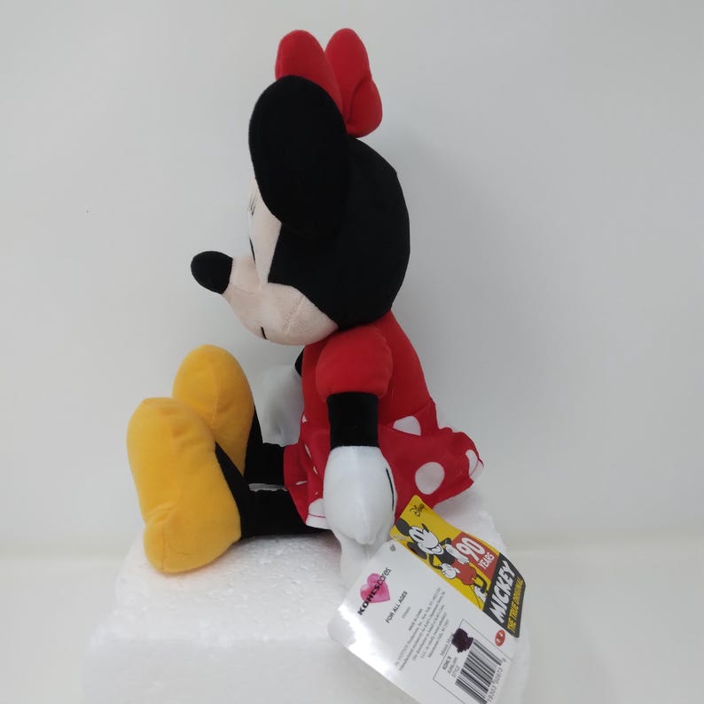 May include: A Minnie Mouse plush toy, featuring a red dress with white polka dots, a red bow, and yellow shoes. The black and white character is sitting with a tag that reads "Mickey 90 Years".