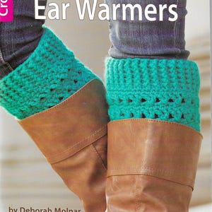 May include: A book cover with a photo of brown boots with teal crocheted boot cuffs and ear warmers. The title of the book is "Boot Cuffs & Ear Warmers" and the author is Deborah Molnar. The book is published by Leisure Arts.