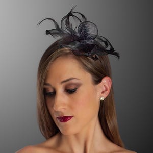 May include: A black headpiece with feathers and netting. The headpiece is worn on the head. The woman in the image is wearing a black strapless top and has long brown hair. She is wearing makeup and a pair of stud earrings.
