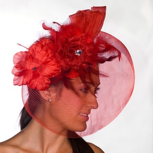 May include: A red mesh hat with a large red flower and a smaller red flower on the side. The hat is decorated with feathers and a rhinestone.