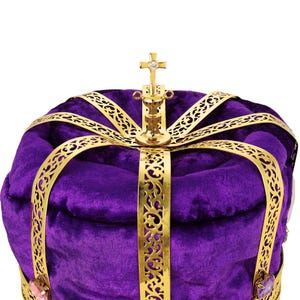 May include: Close-up of a purple velvet crown with gold filigree detailing. The crown features a gold cross at the apex with an inlaid jewel. The rich purple velvet and intricate gold accents create a regal and majestic appearance. This ornate crown is perfect for royalty, theatrical productions, or costume events.