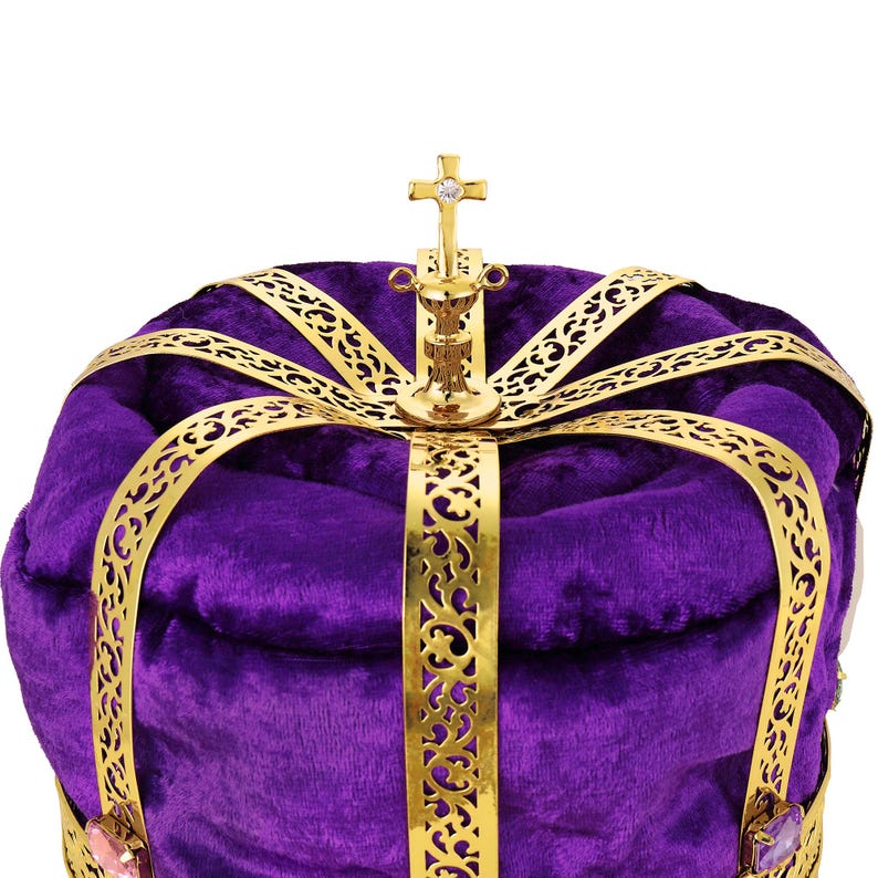 May include: Close-up of a purple velvet crown with gold filigree detailing. The crown features a gold cross at the apex with an inlaid jewel. The rich purple velvet and intricate gold accents create a regal and majestic appearance. This ornate crown is perfect for royalty, theatrical productions, or costume events.
