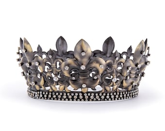 May include: An antique-style crown with a fleur-de-lis design. The crown is made of bronze-colored metal and is adorned with small, sparkling crystals. The base of the crown is lined with additional crystals, adding to its regal appearance.