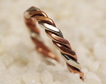 May include: A twisted silver and copper ring, with a braided design. The ring is photographed on a white background.