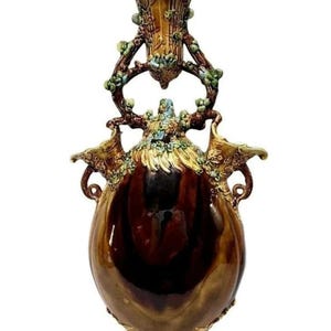 May include: A large, brown ceramic vase with intricate gold and green floral details. The vase has a unique design with a smaller vase on top and two handles on the sides.