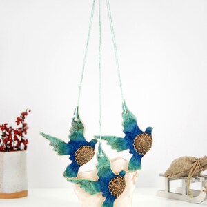 May include: Three ceramic blue and green birds with gold accents hanging from a string. The birds are in flight and have a mandala design on their chests.