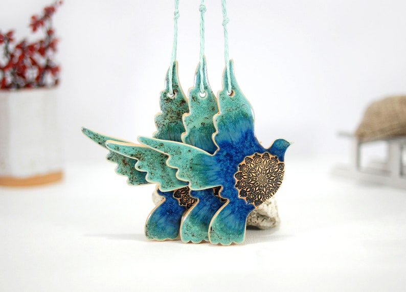 May include: Three ceramic dove ornaments with blue and green glaze and intricate gold details. The doves are hanging from twine.