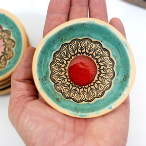 Peut inclure: Un ensemble de petits plats en c&eacute;ramique avec un gla&ccedil;age turquoise et des motifs floraux noirs. Le centre de chaque plat est orn&eacute; d'un cercle rouge.