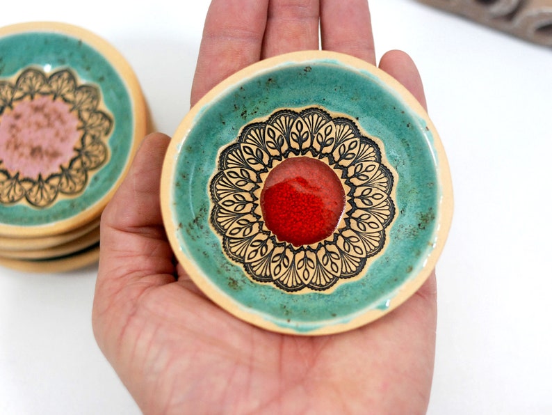 Peut inclure: Un ensemble de petits plats en c&eacute;ramique avec un gla&ccedil;age turquoise et des motifs floraux noirs. Le centre de chaque plat est orn&eacute; d'un cercle rouge.